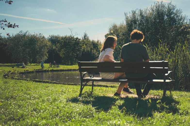 two people sitting on a bench by a pond