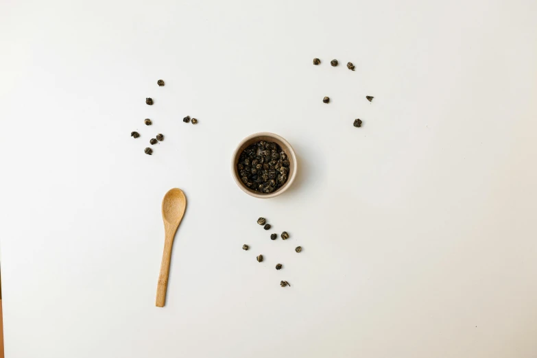 a wooden spoon with black pepper seeds and spoon on white surface