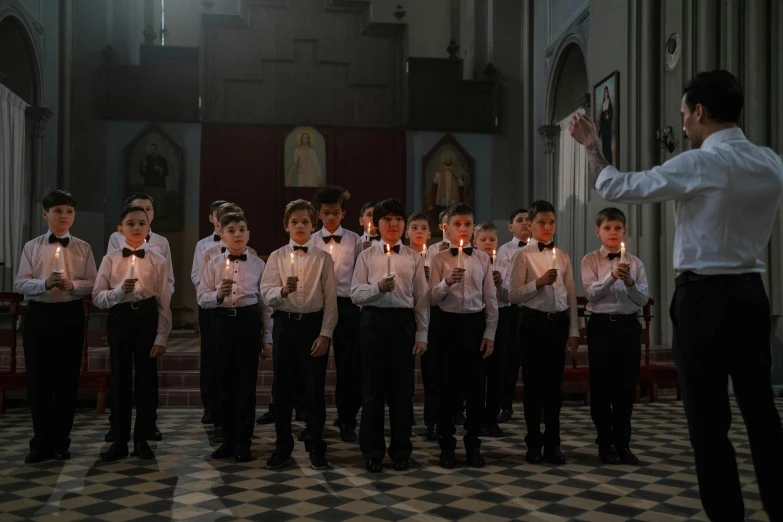 a choir of boys holding candles stands by a priest