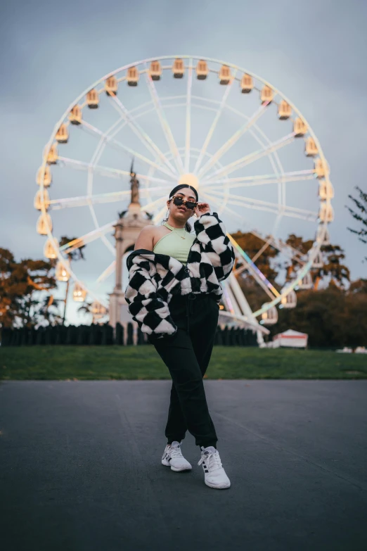 woman wearing checkered jacket and hat posing with large ferris wheel