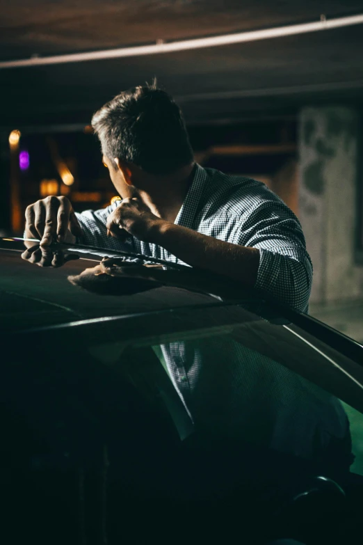 man in dark car gazing over window while rubbing up against the hood