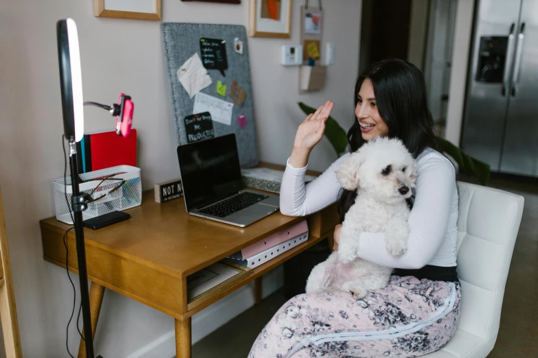 a young woman is sitting on the desk with a white dog in her lap