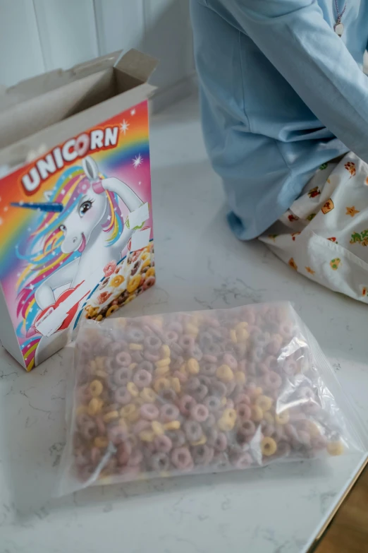 the girl is putting cereal in the bag with the unicorn box beside her