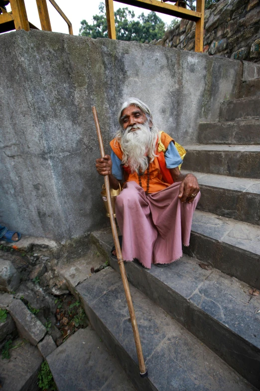 man sitting in front of stairs holding long stick