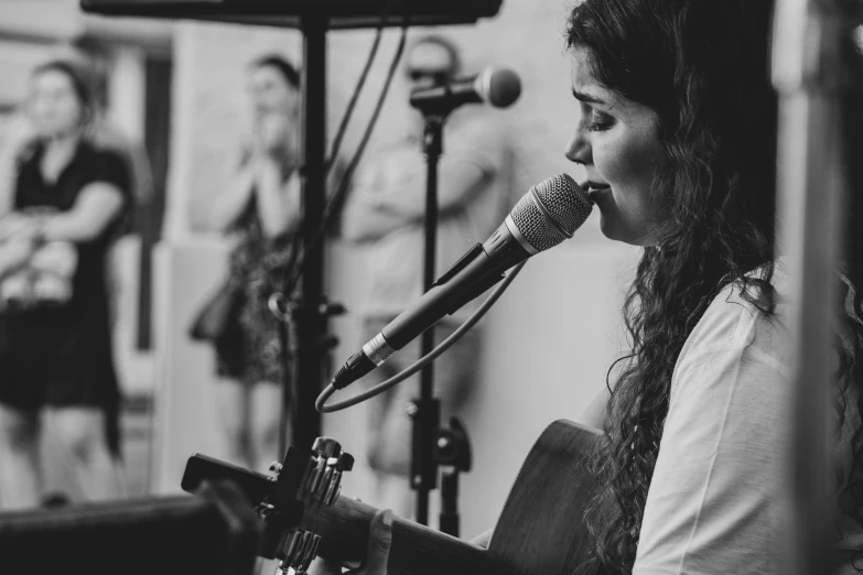 woman singing into a microphone while playing the guitar