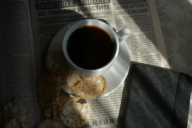 a cup of coffee and some biscuits on a newspaper