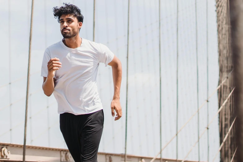 man in white t - shirt and black pants running over a bridge