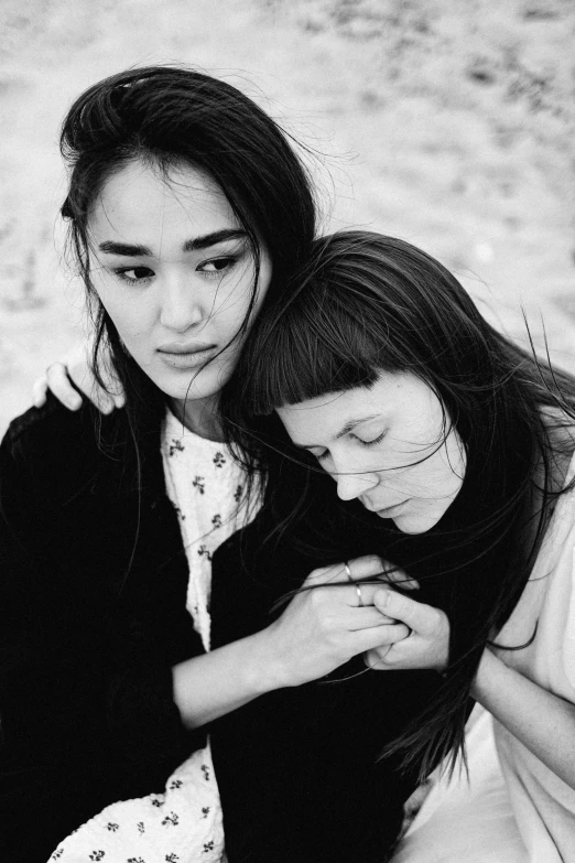 two women sit near one another on the beach and one is touching her face