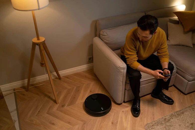 a man in a yellow sweater sits on a couch looking at his cellphone
