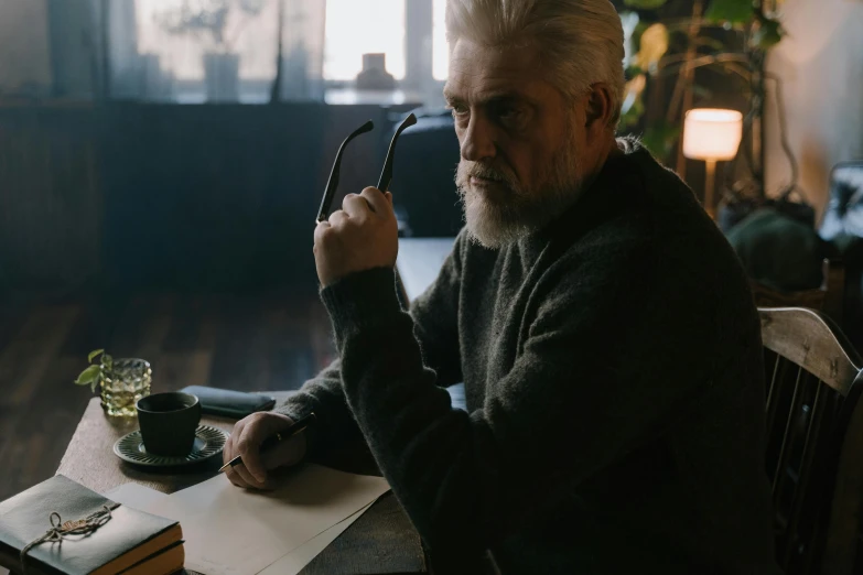 an elderly man writing on a notebook in front of a lamp