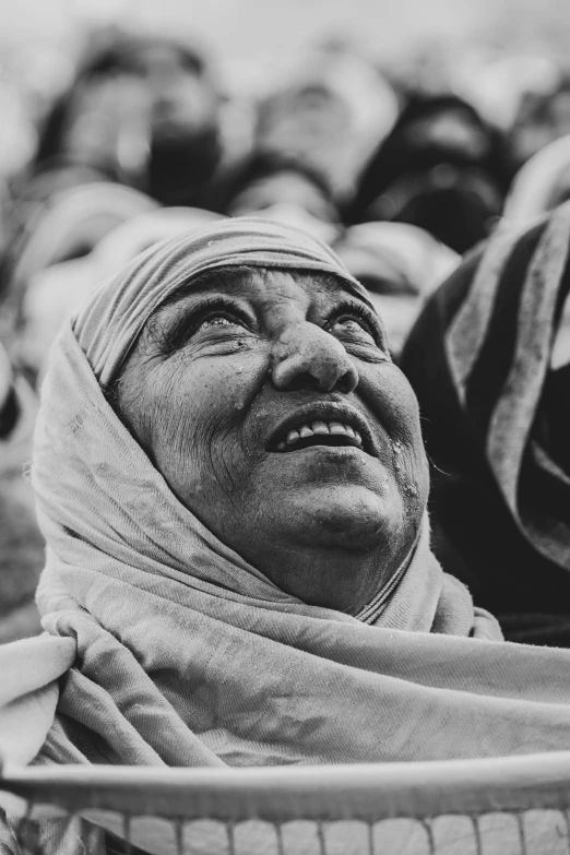 an old woman wearing a headscarf looks up into the sky