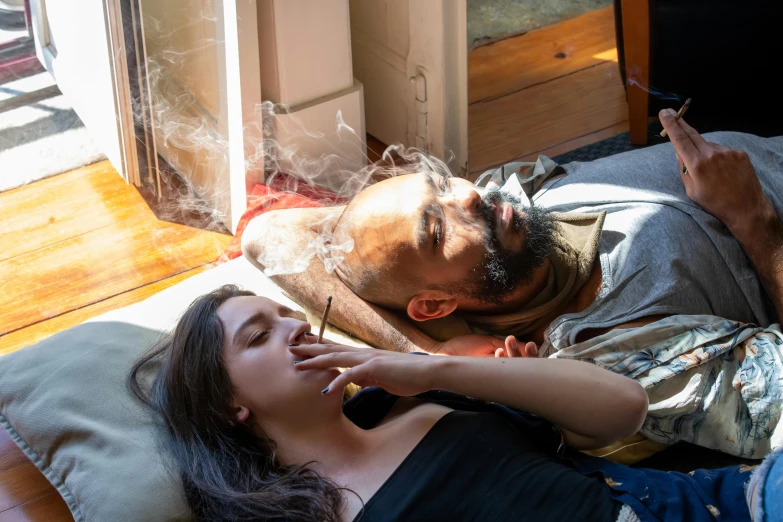 a woman laying down smoking in bed next to a man