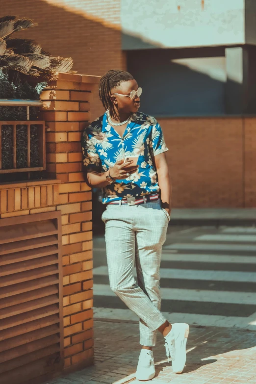 an african man wearing sandals stands against a brick wall