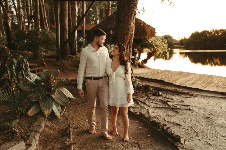 a man and woman standing next to a tree on a beach