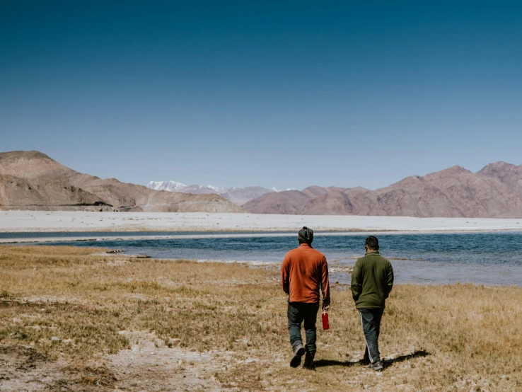 two men standing in the grass and looking at some mountains