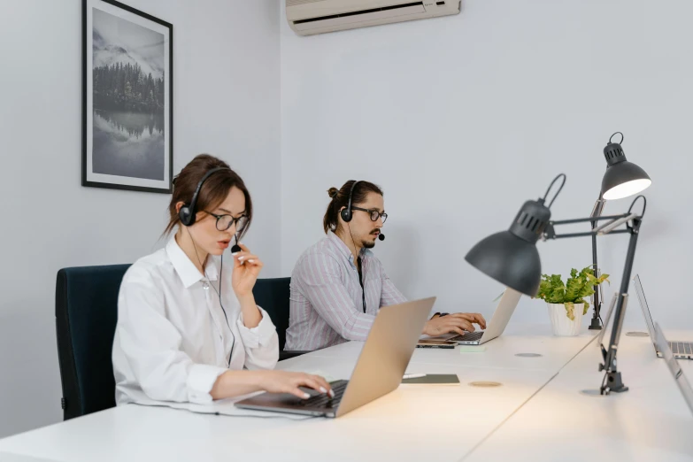 two people with headset sit at a desk working on their laptops