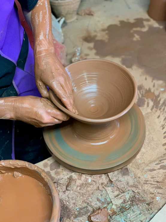 a person wearing gloves holds a brown clay vessel