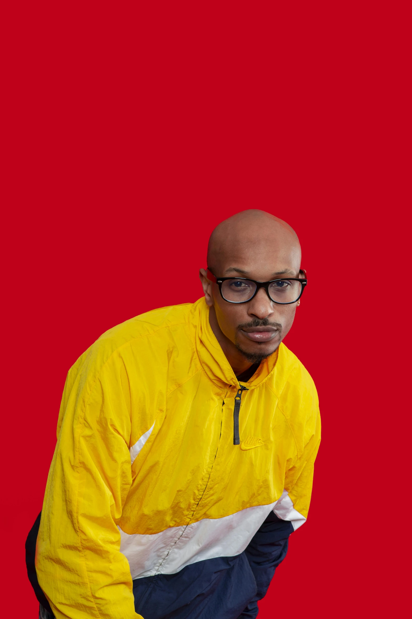 a man with glasses is standing near a red background