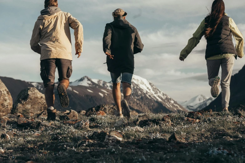 three people in hiking gear are running across the grass