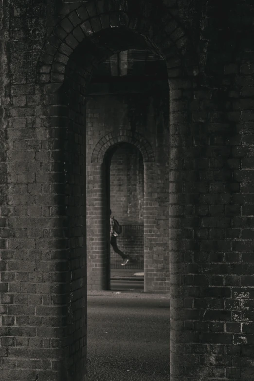 black and white image of person coming out from an alleyway through brick pillars