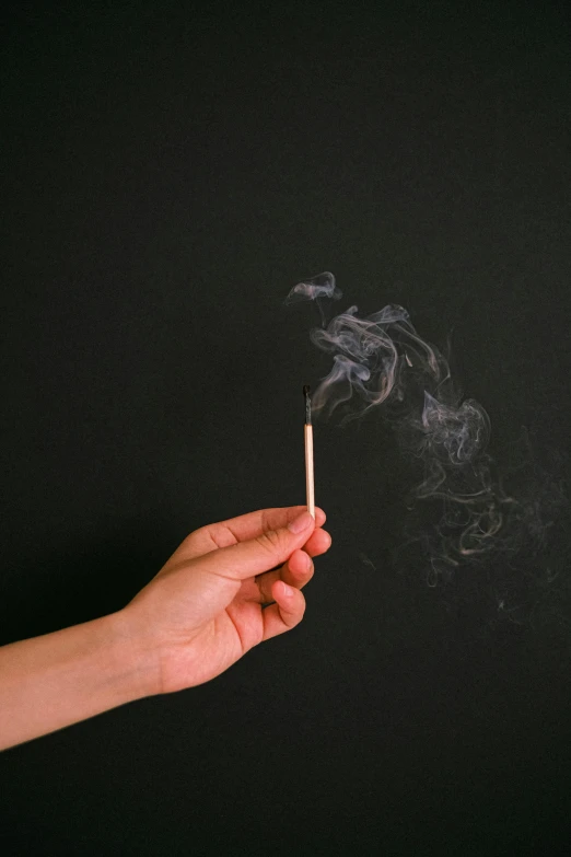 a persons hand holding a cigarette that has just been lit