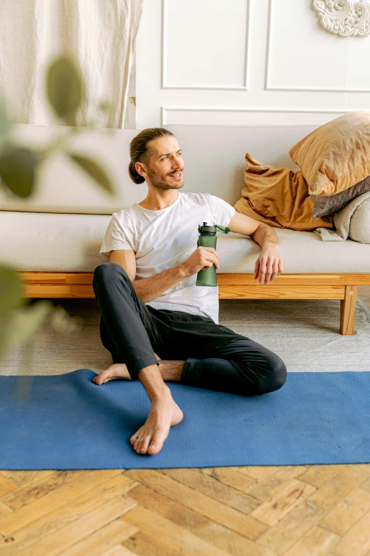 a man is sitting on a yoga mat holding a coffee cup