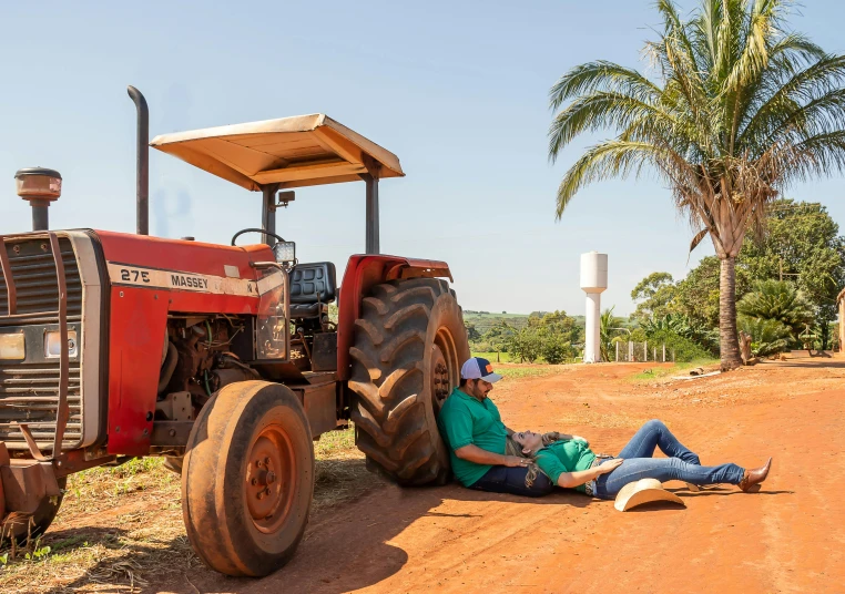 a man lies on the ground beside a tractor and has his leg up against another man as he lays on the road