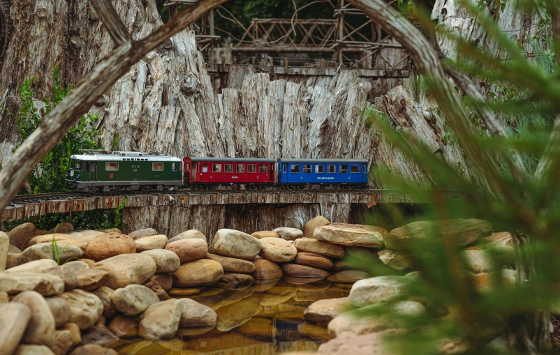 a model train with a red one going over a bridge