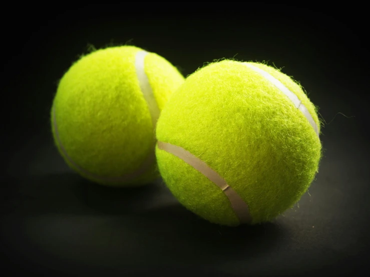 two tennis balls are sitting on a black surface