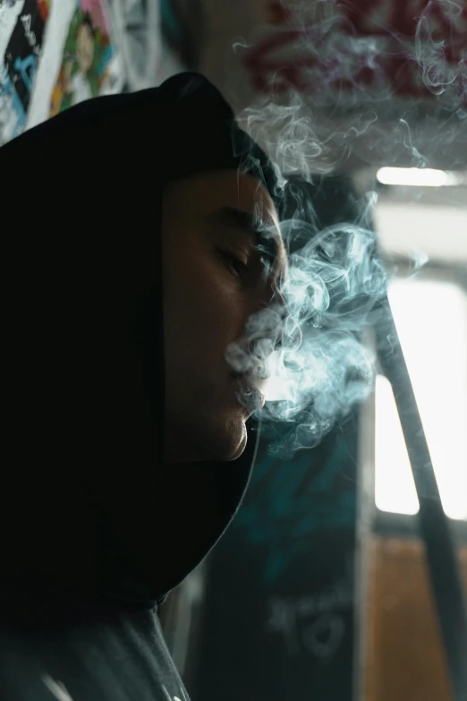 a man wearing a hooded sweatshirt and smoking a cigarette