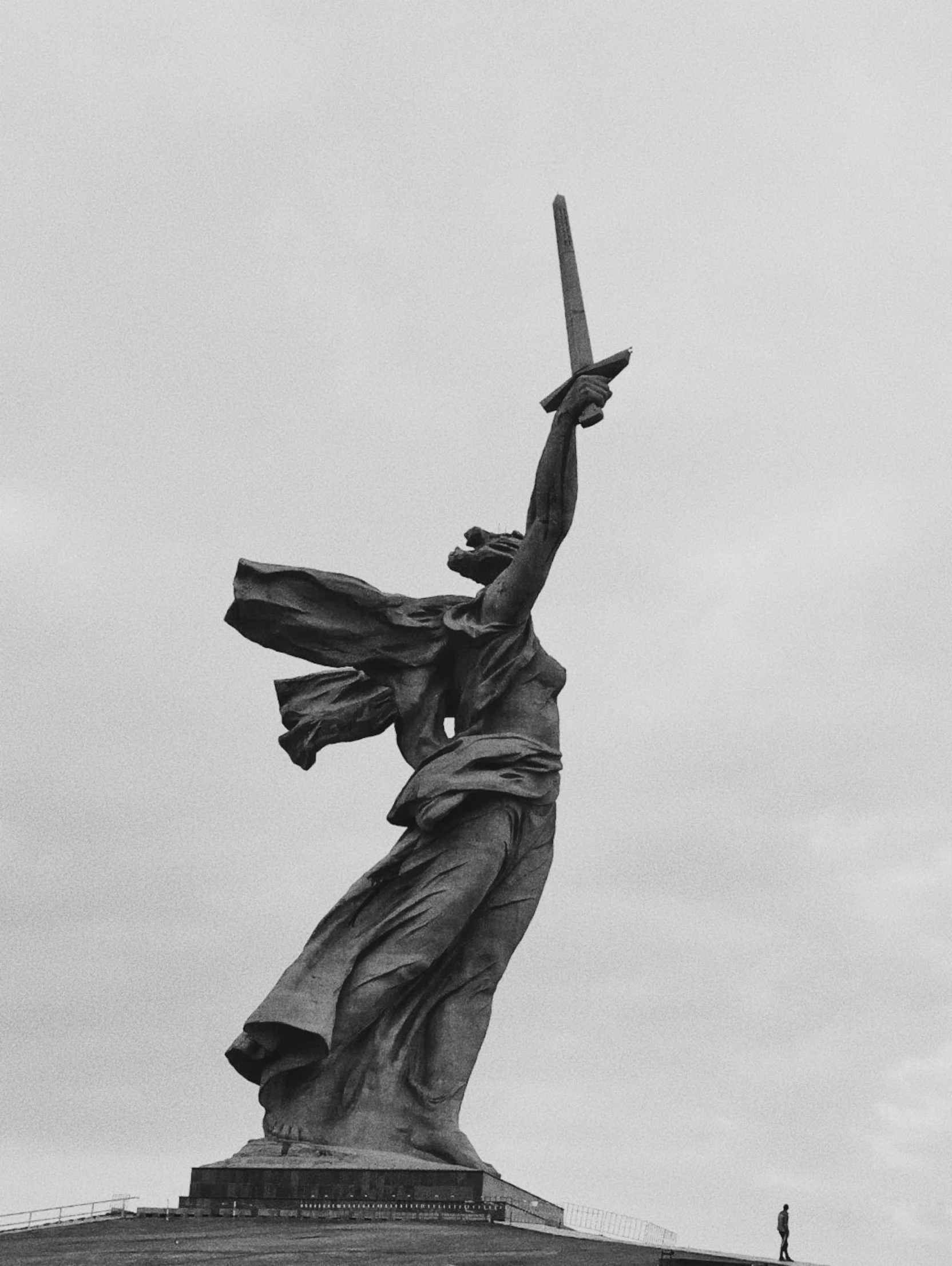 a woman holding a sword up to the sky near a statue