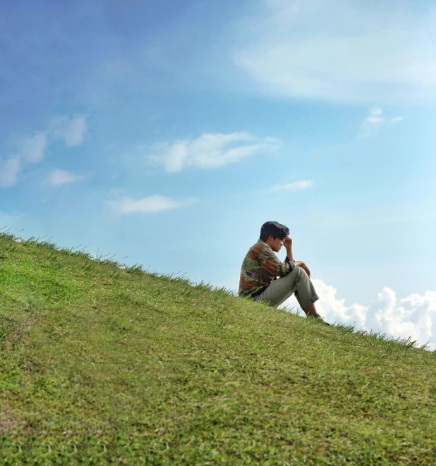 a man is sitting on the hill with his phone to his ear