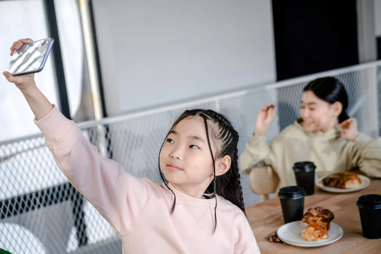 a little girl reaching up to take a picture with her cell phone