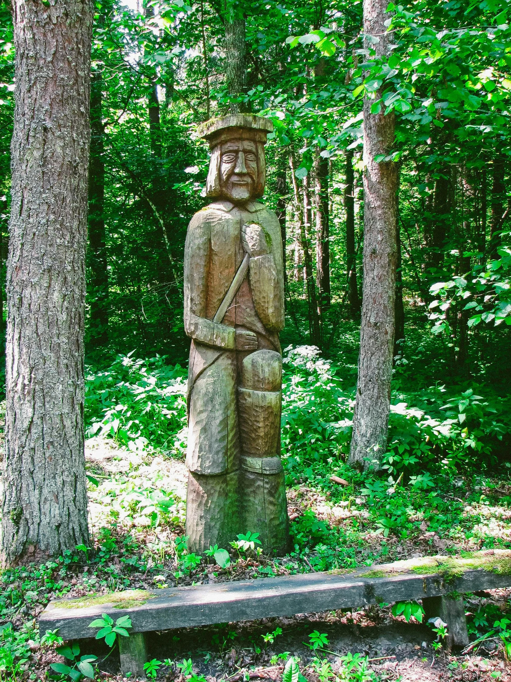 a small wood statue standing in the middle of some trees