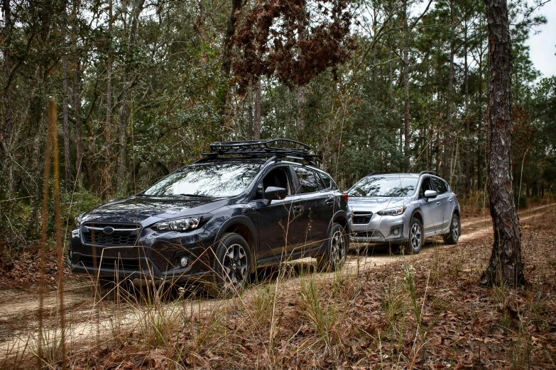 two vehicles sitting on a dirt road in a wooded area