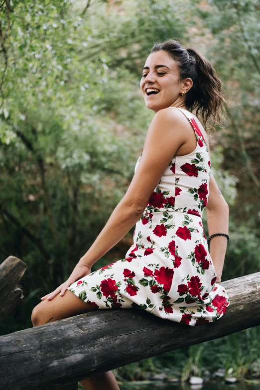 a girl in a dress sitting on a log looking to her right with eyes closed