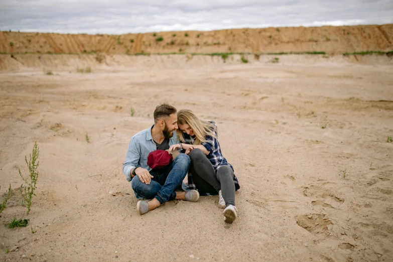 a man and woman are sitting in the sand, each holding the other