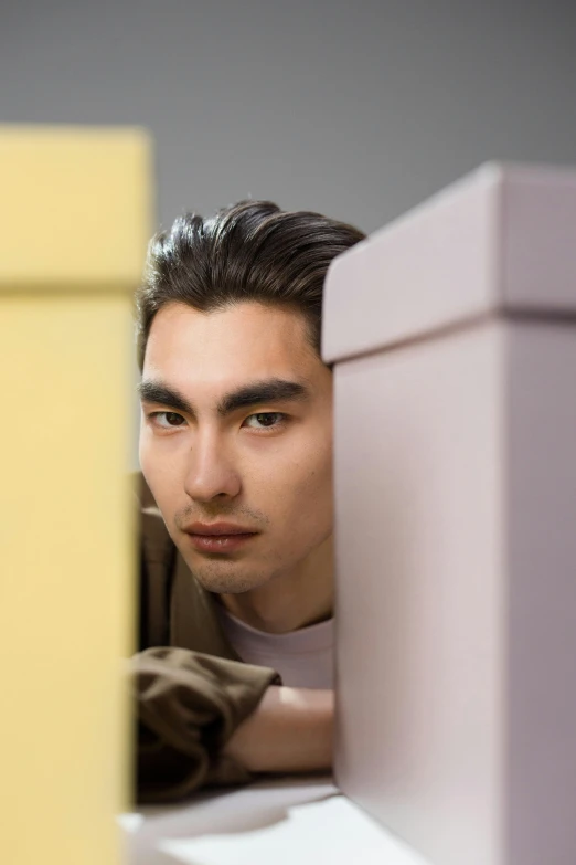 man in brown jacket leaning against the side of a yellow wall