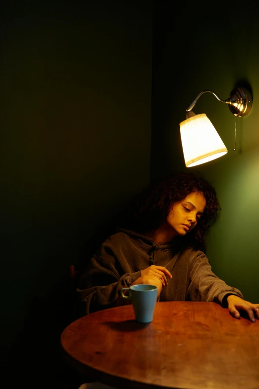 a woman sitting at a table with a coffee cup under a lamp