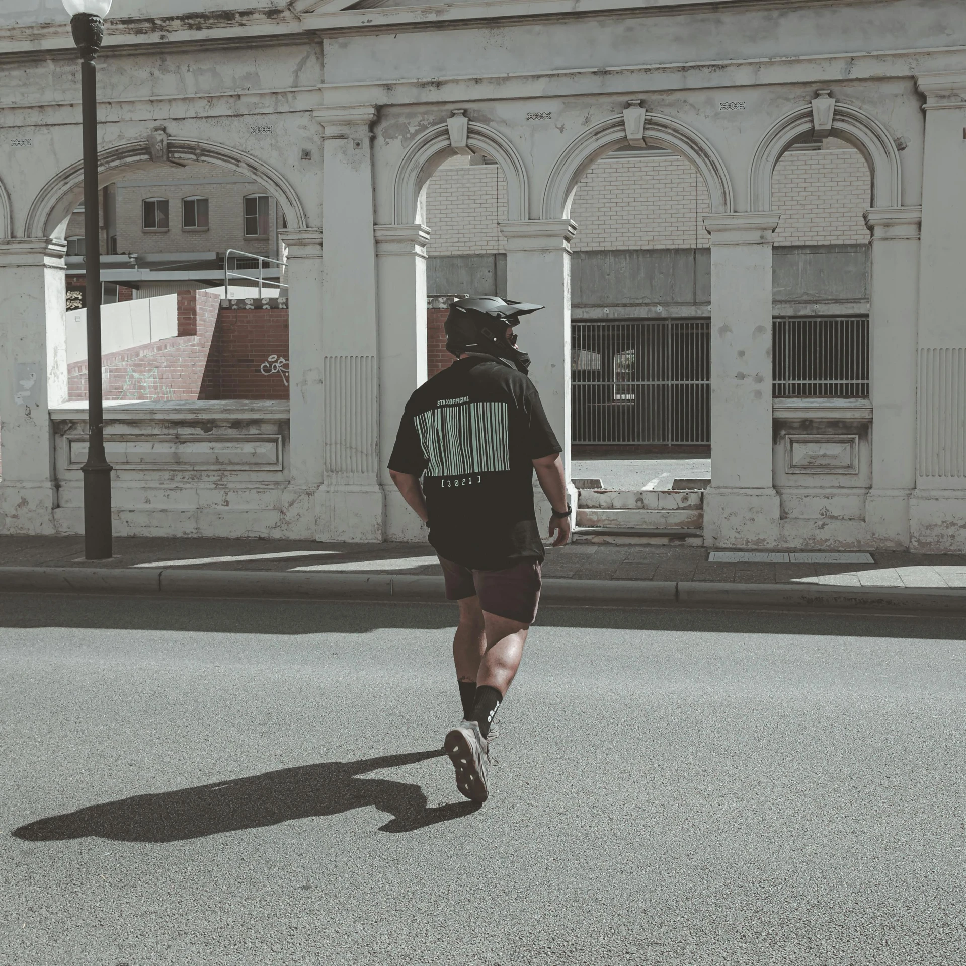 a person with a shirt that reads iron cross is on the road near a building