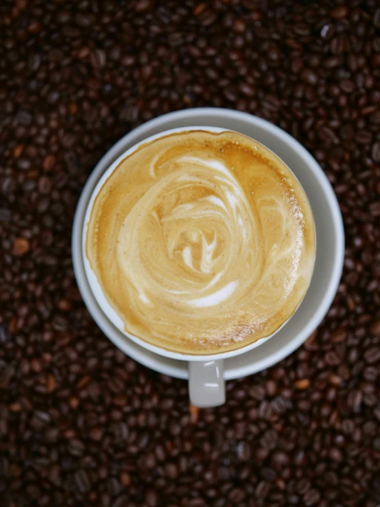 top view of a cappuccino in a white saucer on a coffee bean background