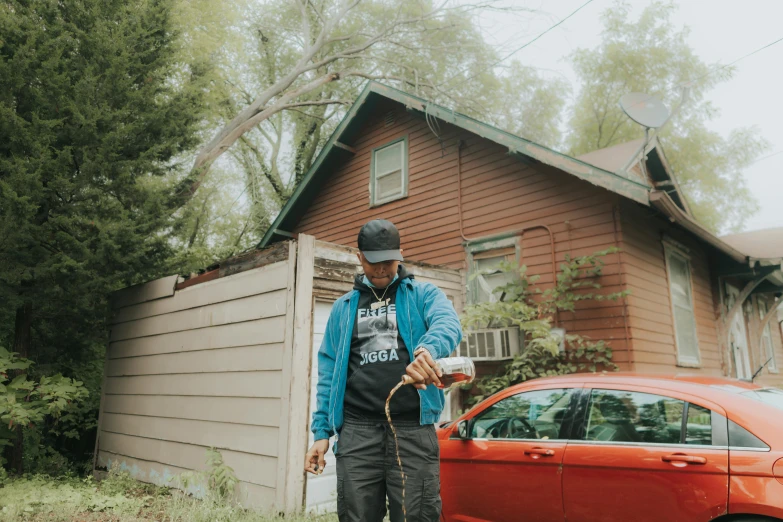 a man stands next to a red car and uses a piece of paper