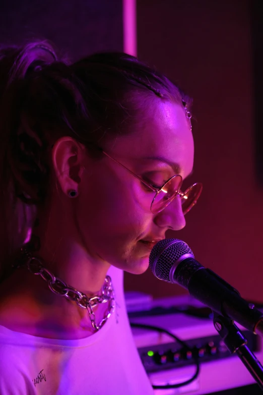 a woman singing into a microphone in front of purple lighting