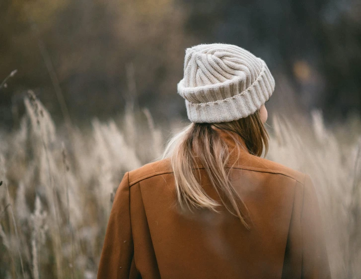 a woman with a sweater and hat walks through tall grass