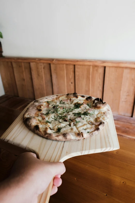 someone holding a pizza over a wooden table