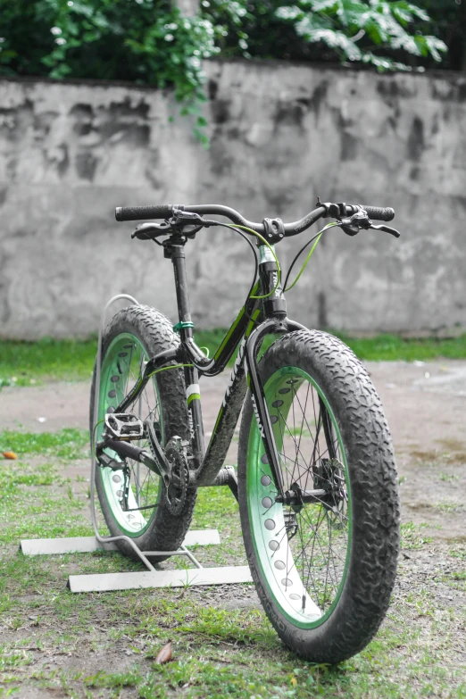 a green and black bicycle sitting on some dirt