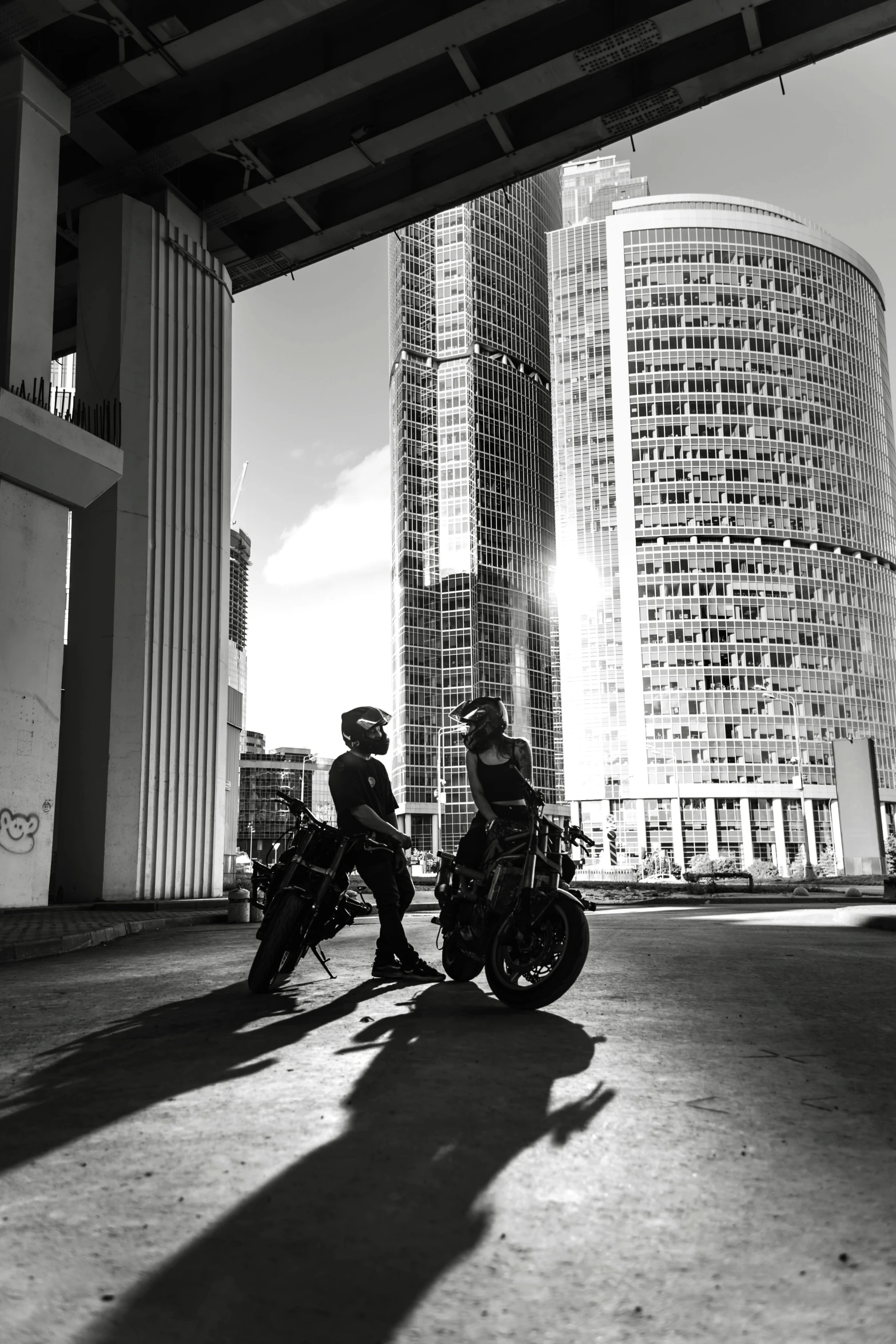 two people on motorcycles sitting under a bridge