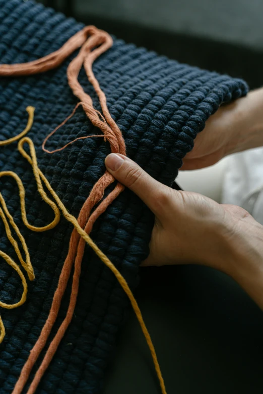 a hand stitches a cord on to a piece of fabric