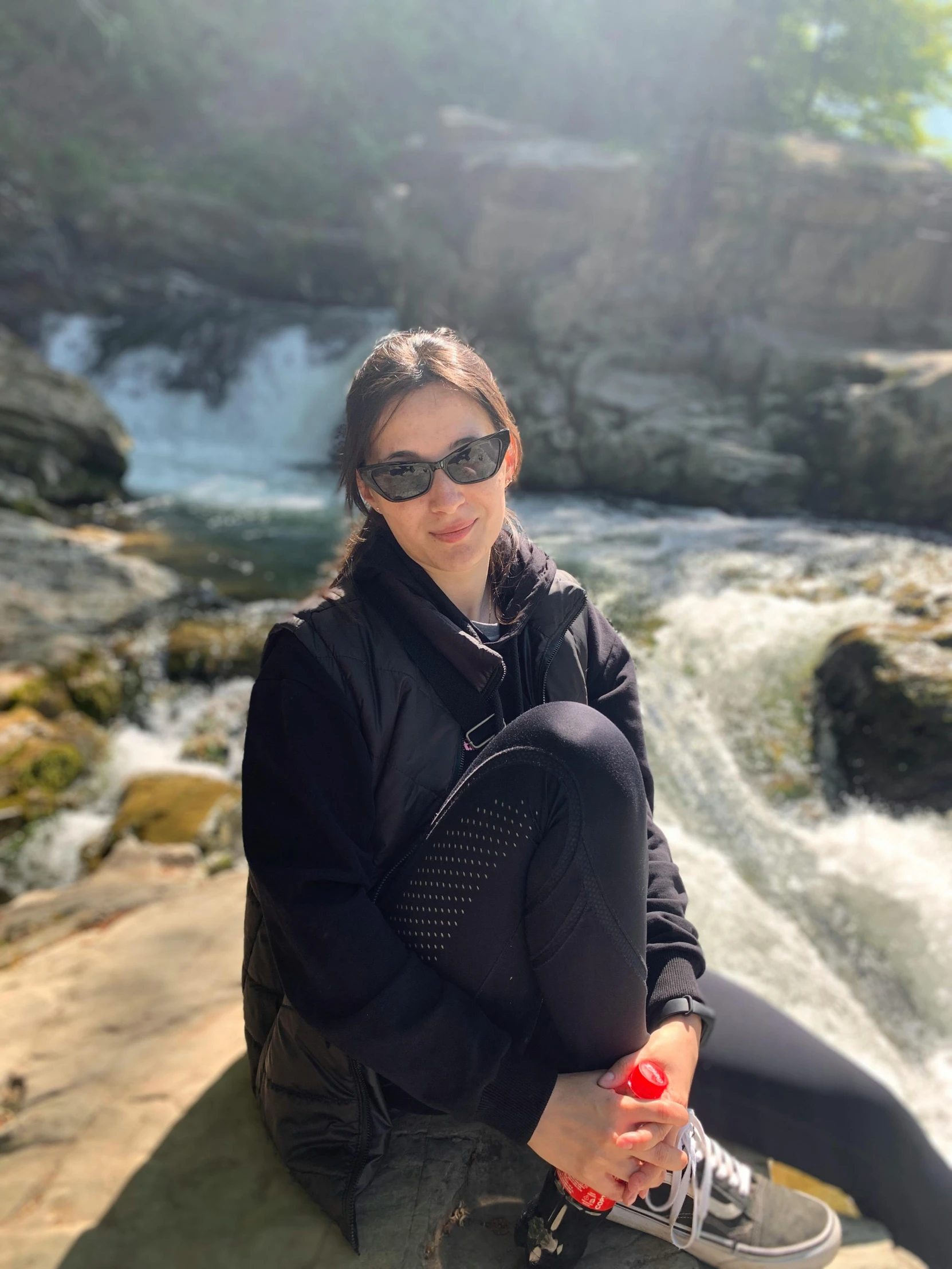 a young woman sitting on a rock in front of water