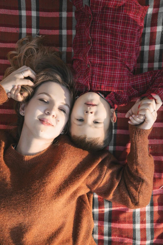 a  lays on a red checkered comforter with her face pressed behind a man who is holding his head in his hands